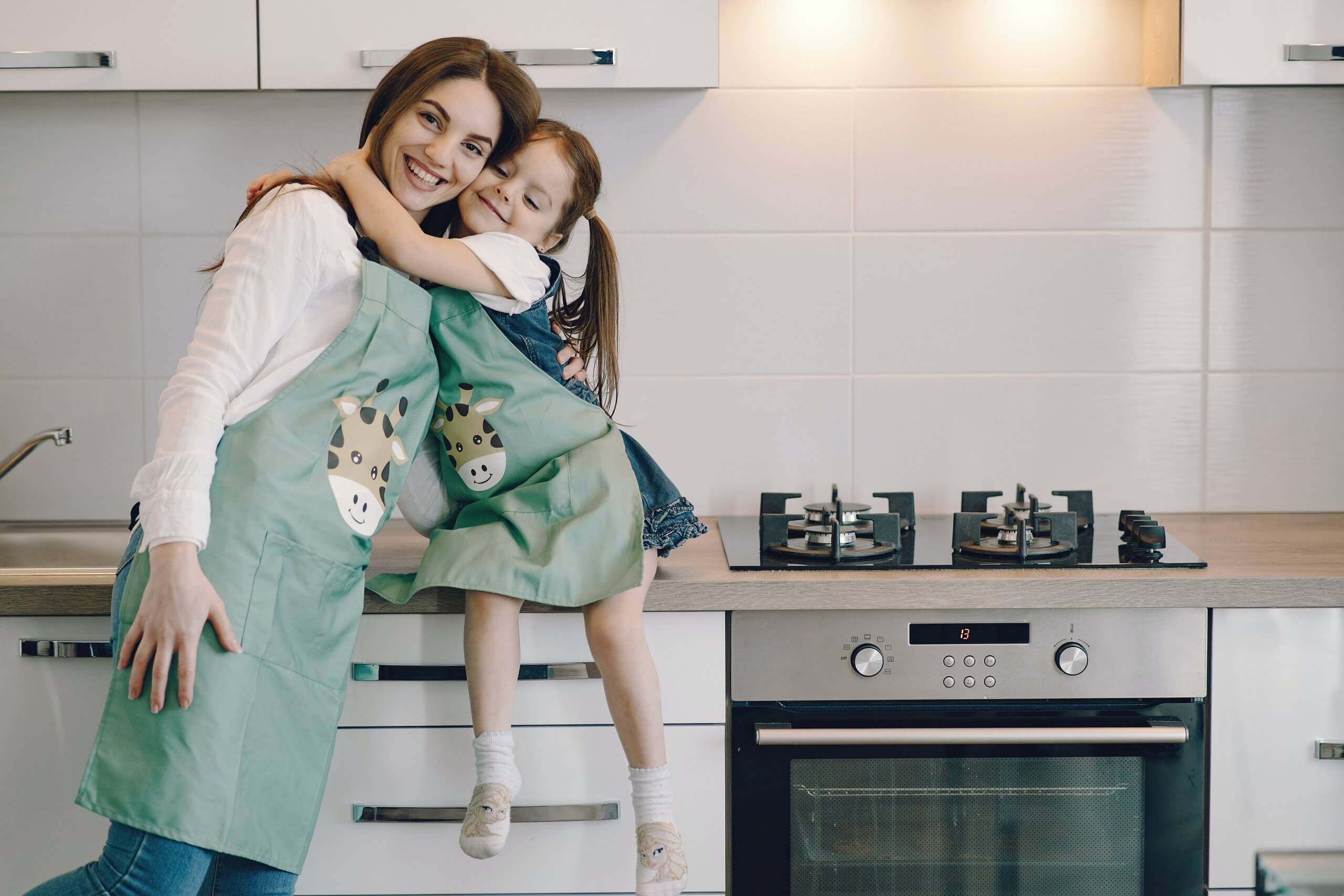 mãe e filha abraçadas na cozinha vestidas com aventais