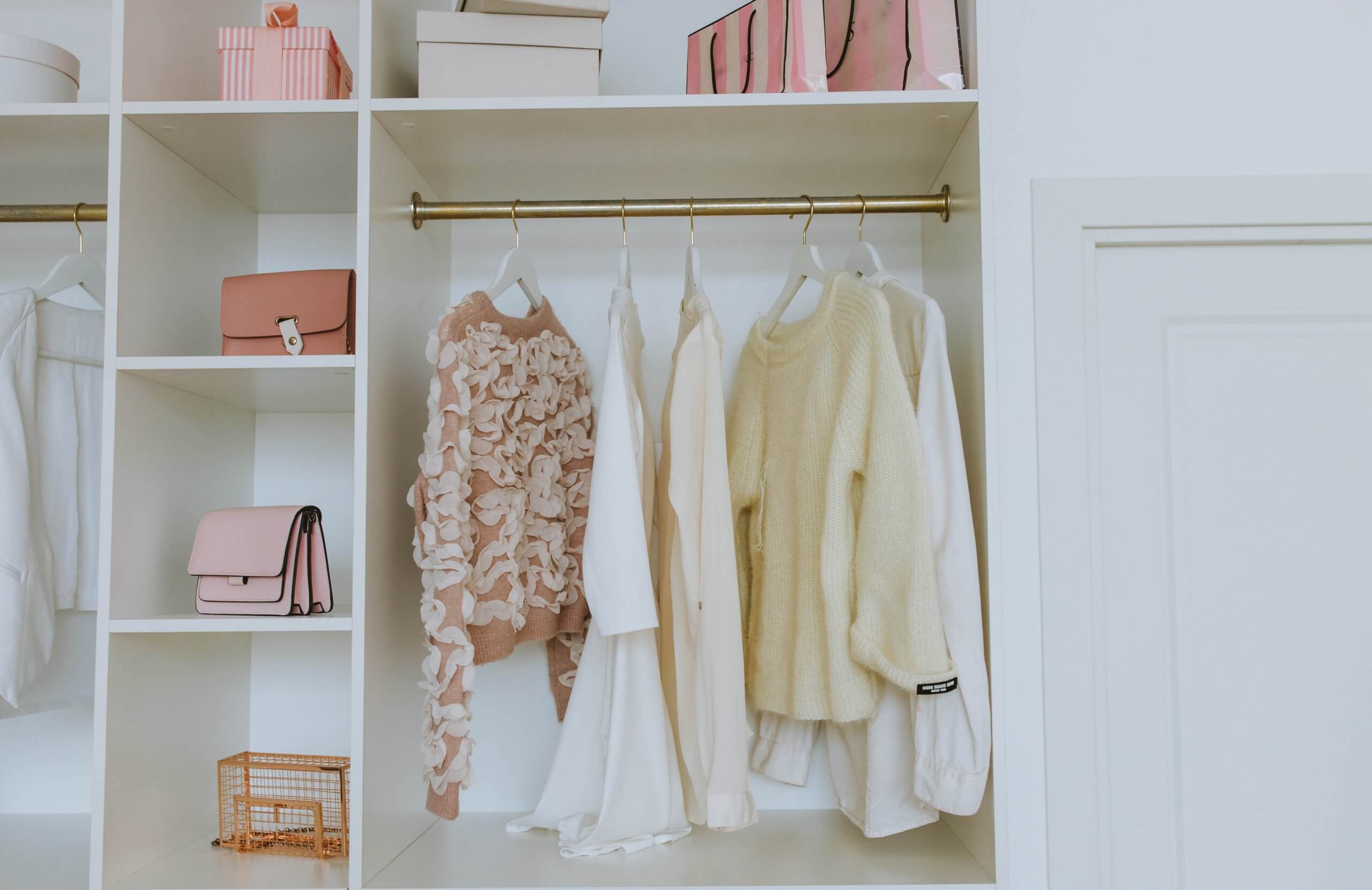 armário branco com roupa de mulher pendurada de cor de rosa e branco e malas em prateleiras